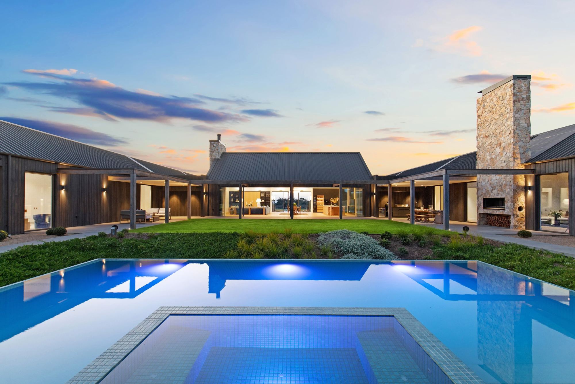 Architect-designed home at dusk, lit pool in the foreground